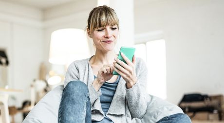 Eine Person liegt am Strand auf einer Liege und informiert sich über Card Control auf dem Smartphone.