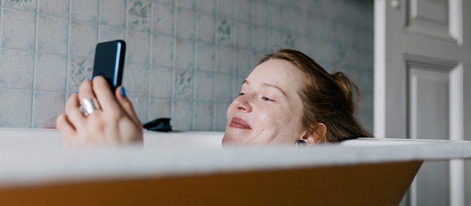 Frau badet und schaut in ihr Smartphone