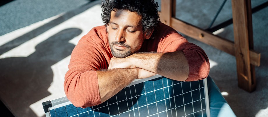 Mann stützt sich an Solarpanel und genießt die Sonne