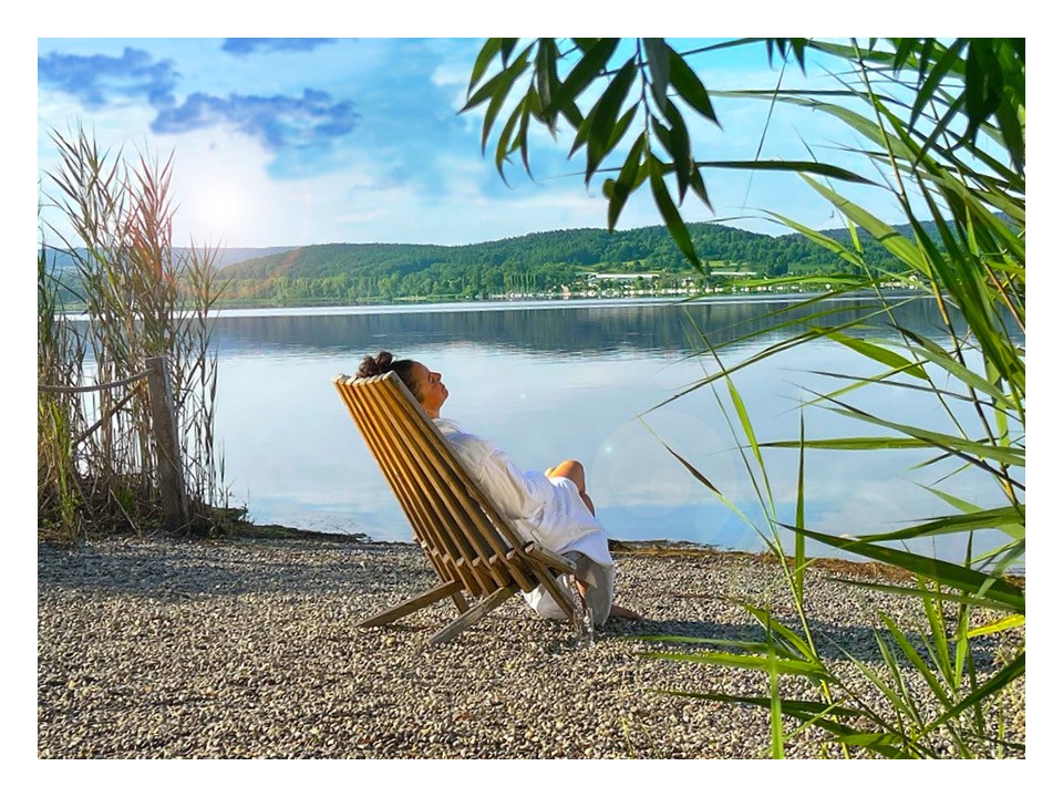 Frau auf einem Liegestuhl und im Bademantel am See