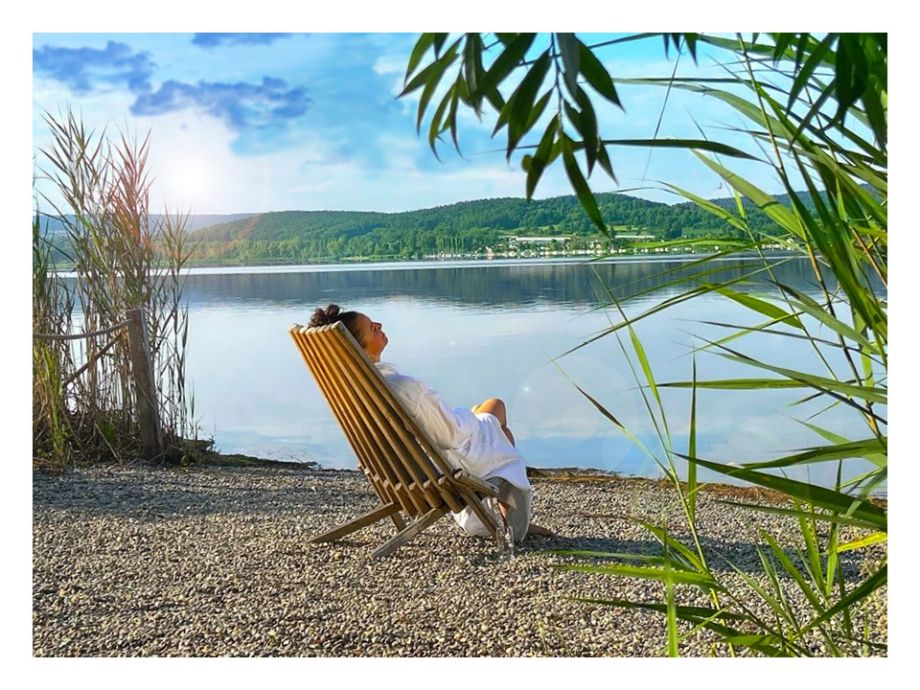 Frau auf einem Liegestuhl und im Bademantel am See